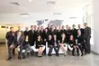 Group photo of a professional corporate team in business attire, posed in a modern office lobby with a world map on the wall in the background.